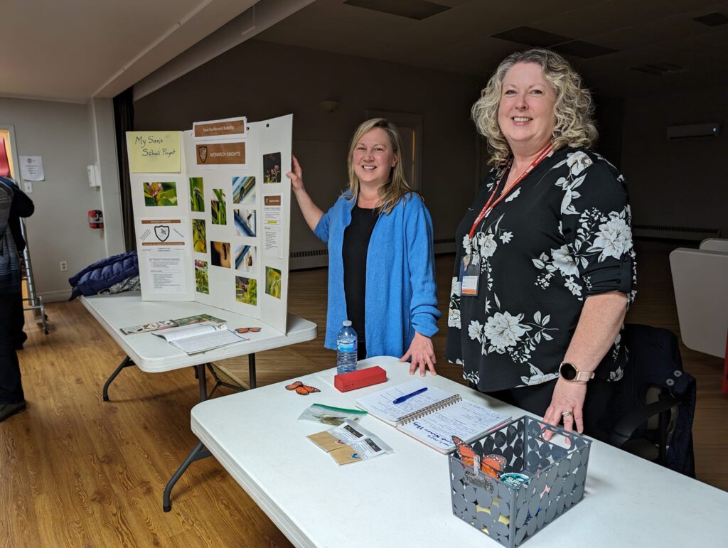 Volunteers with the Sackville Photography Club smiling at an event table, sharing educational displays and club information.